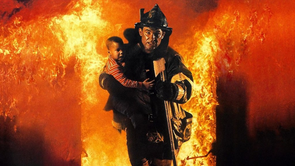 Man in fire brigade unform grips a baby and runs through fire